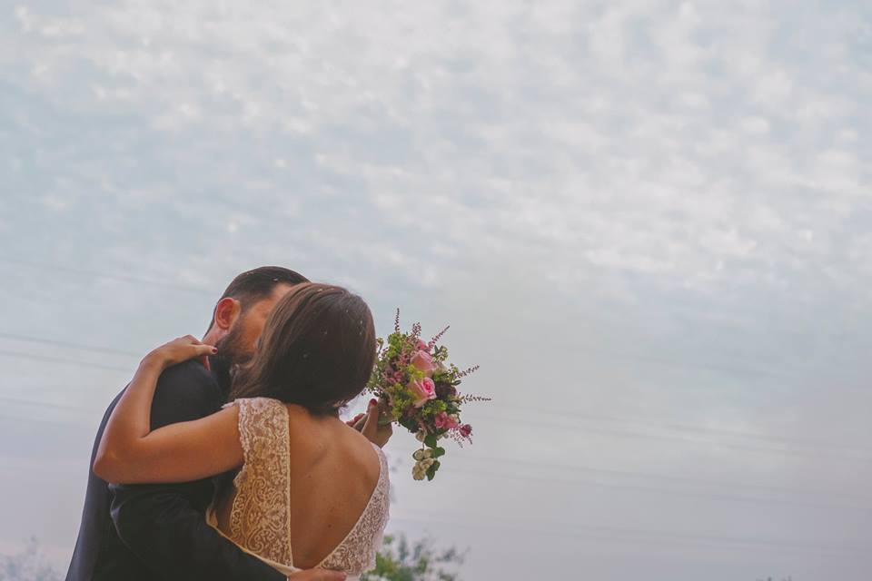 Novio y novia se dan un beso mientras el chico sostiene un ramo de flores de la floristería crisálida en elche.