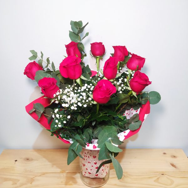 Ramo premium de 12 rosas rojas intensas con paniculata blanca y eucalipto, presentado en jarrón decorado con corazones