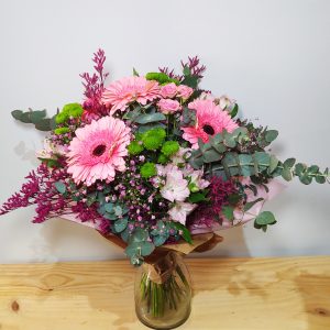 Exuberante ramo con gerberas rosas, mini crisantemos verdes y astilbe fucsia, complementado con eucalipto, presentado en jarrón de cristal